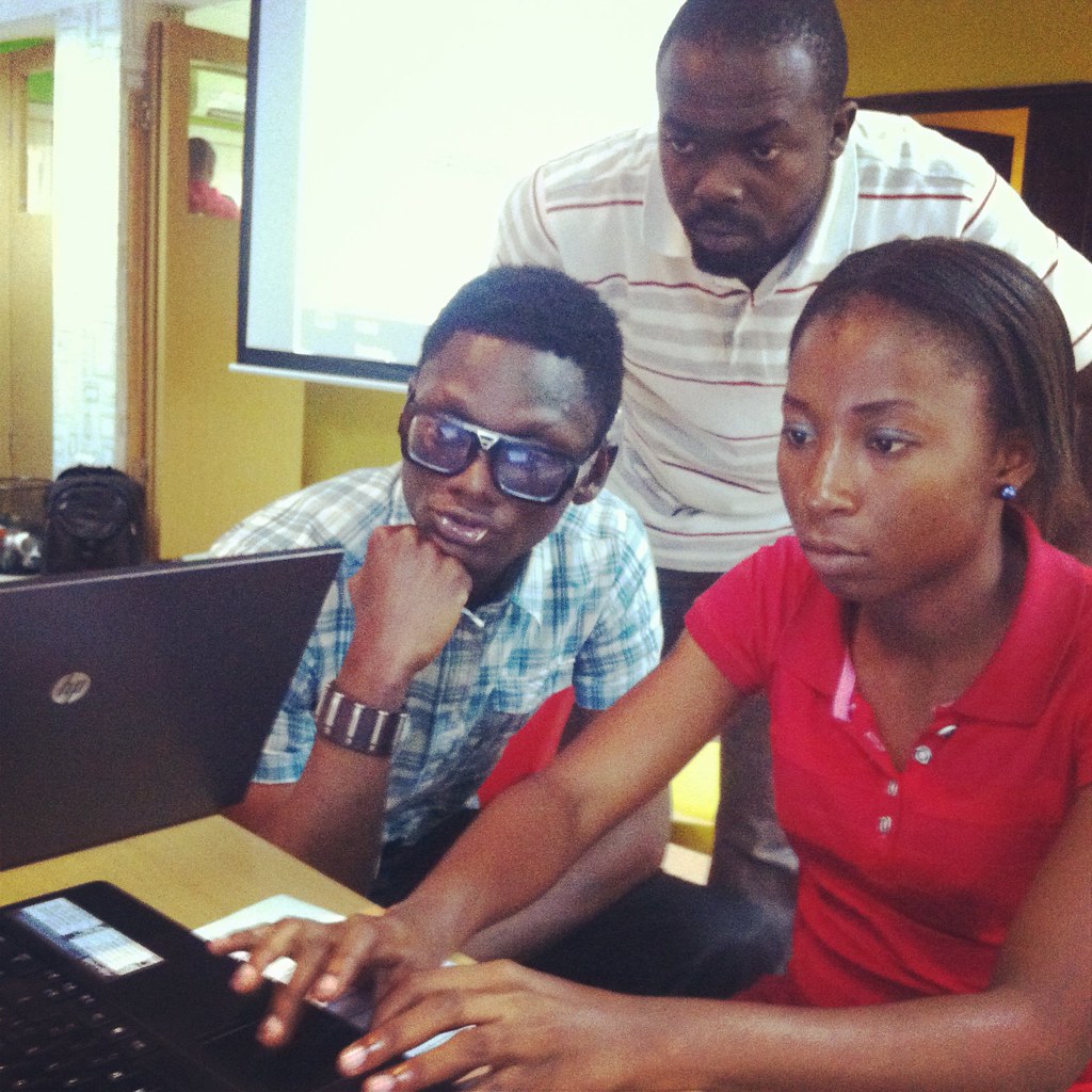 Three young people gathered around a laptop looking at the screen
